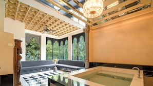A luxurious bathroom with a large bathtub, a checkered floor, and a seating area with a view of greenery.