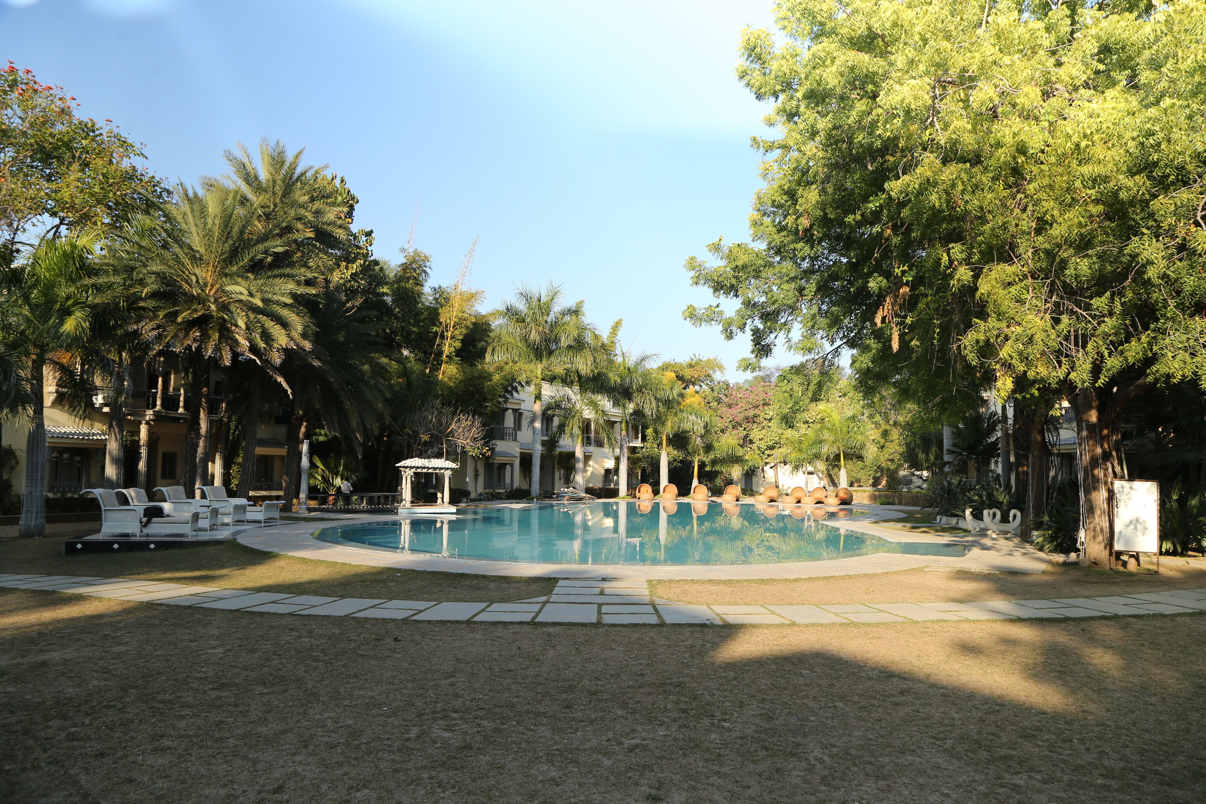 Un área de piscina con sillas de descanso, palmeras y un pabellón.