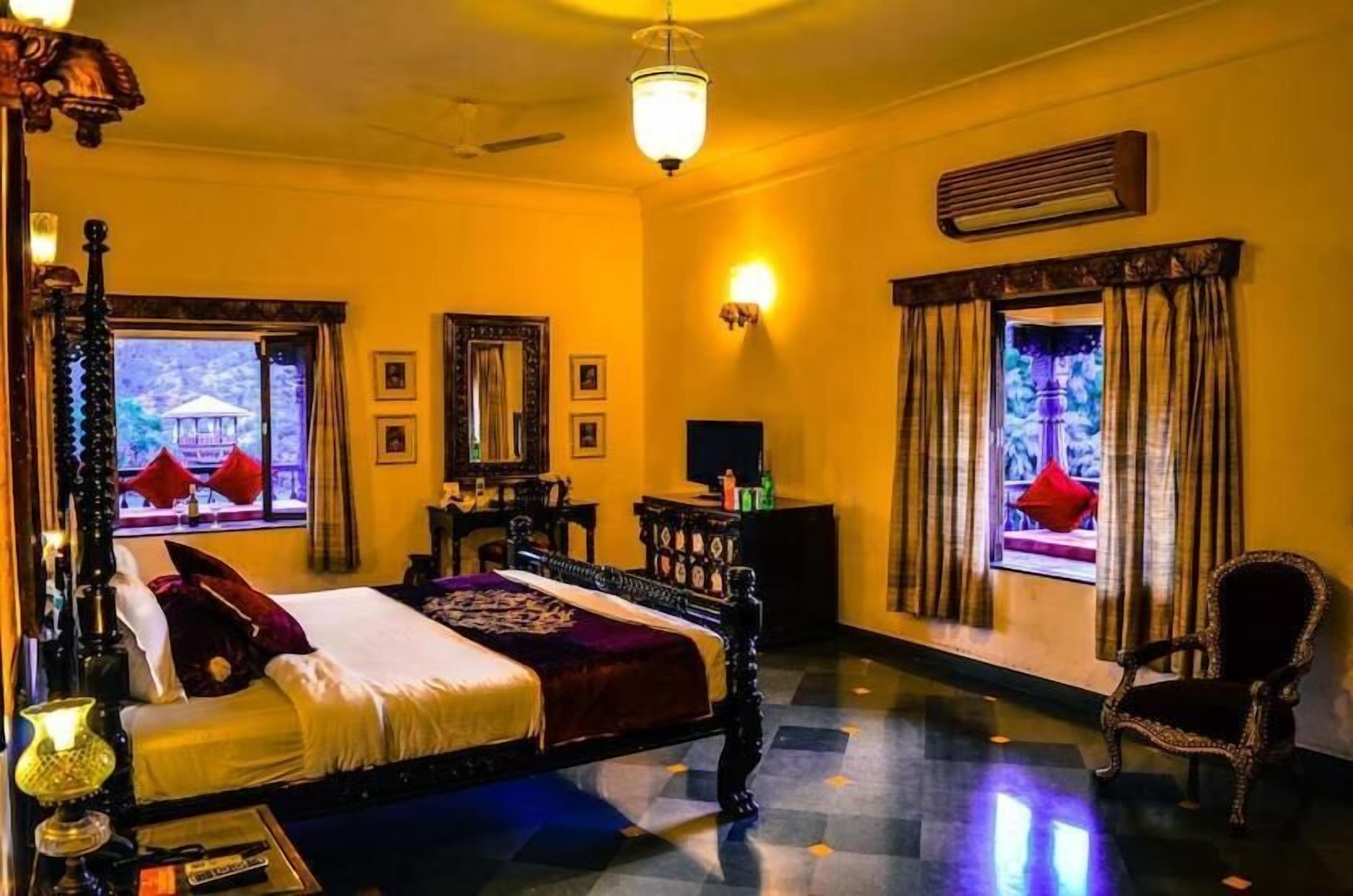 Ein Hotelzimmer mit Bett, Stuhl, Schreibtisch, Lampe und einem fensterbepflanzten Fenster.