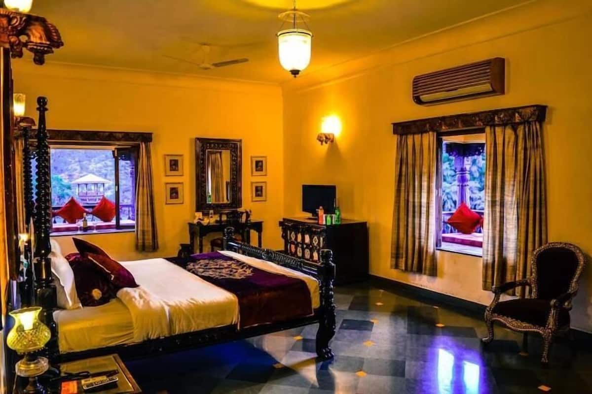 Habitación de hotel con cama, silla, escritorio, lámpara y ventana con cortinas.
