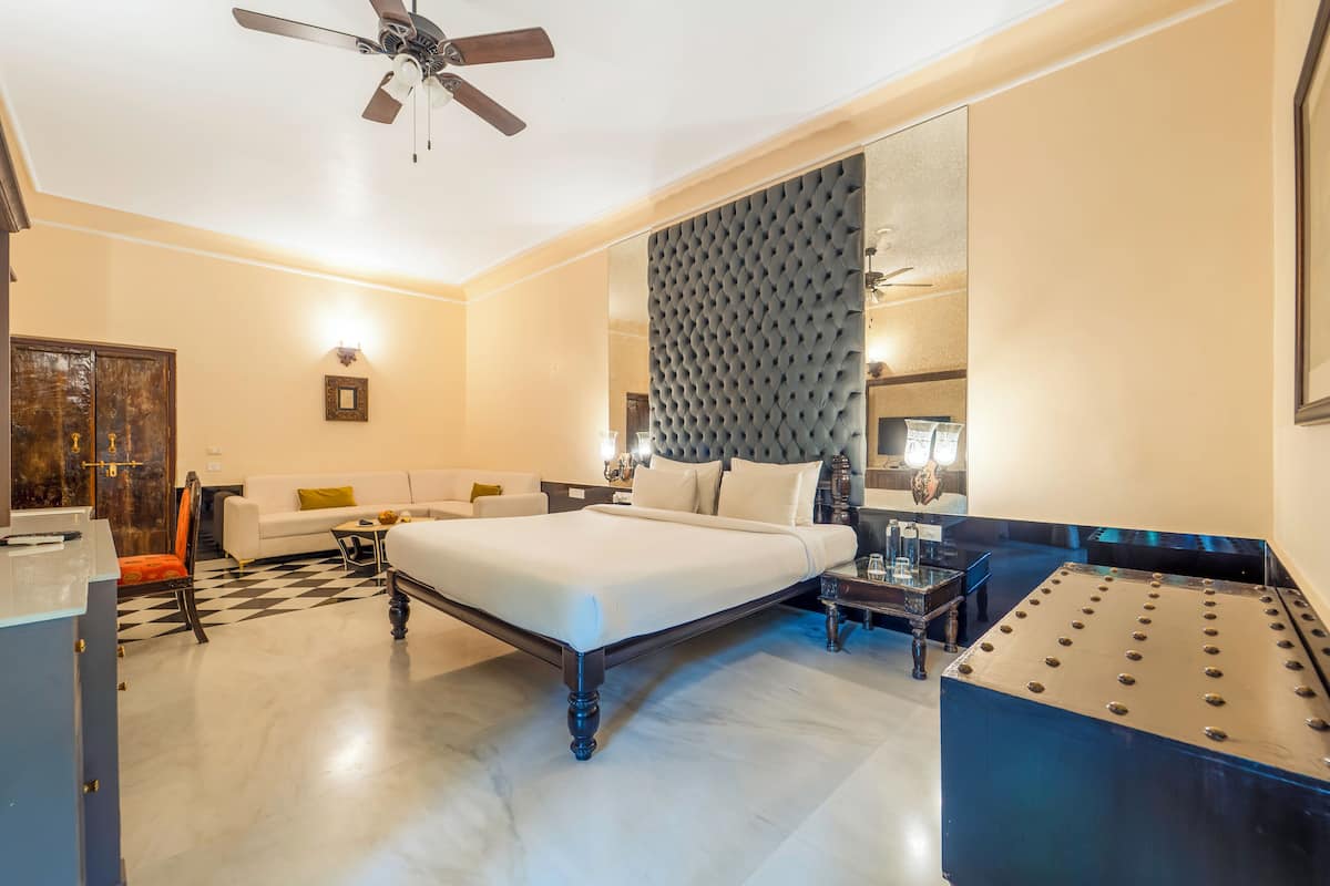 Una habitación de hotel moderna con una cama grande, una zona de estar con sofá y sillones, una mesita y un ventilador de techo.