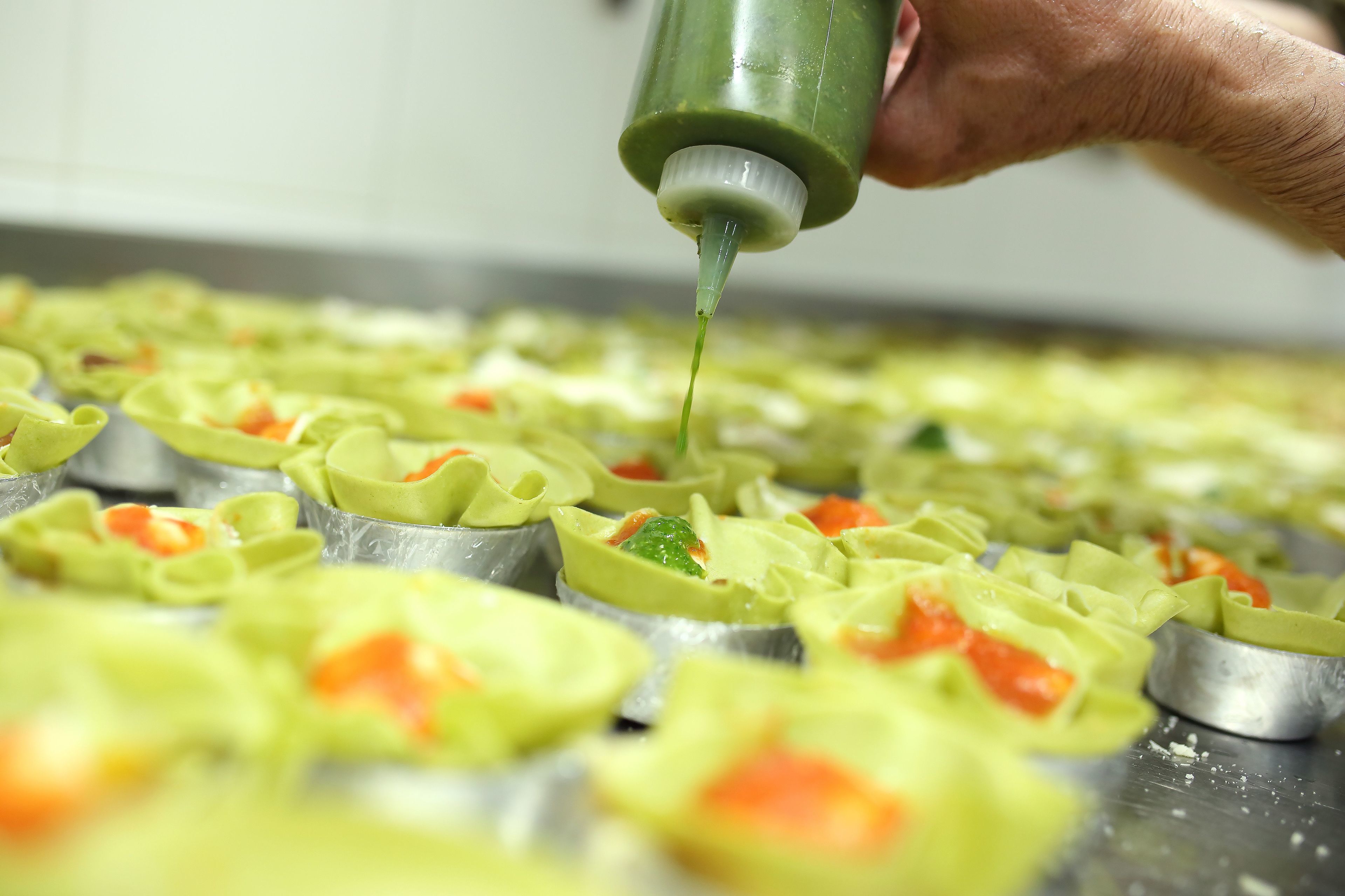 A person pouring a green substance onto food items on a tray.