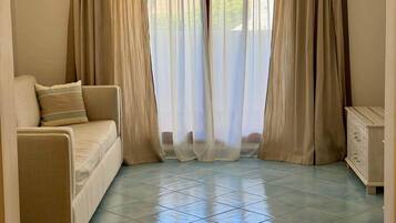 Una camera d'albergo con un letto, un divano, un piccolo armadio e tende leggere.