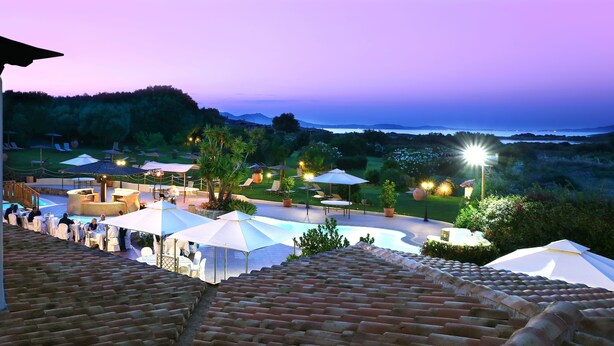 A terrace with outdoor seating and umbrellas, overlooking a landscaped garden and a body of water. - Hotel Sa Pedra (Olbia)