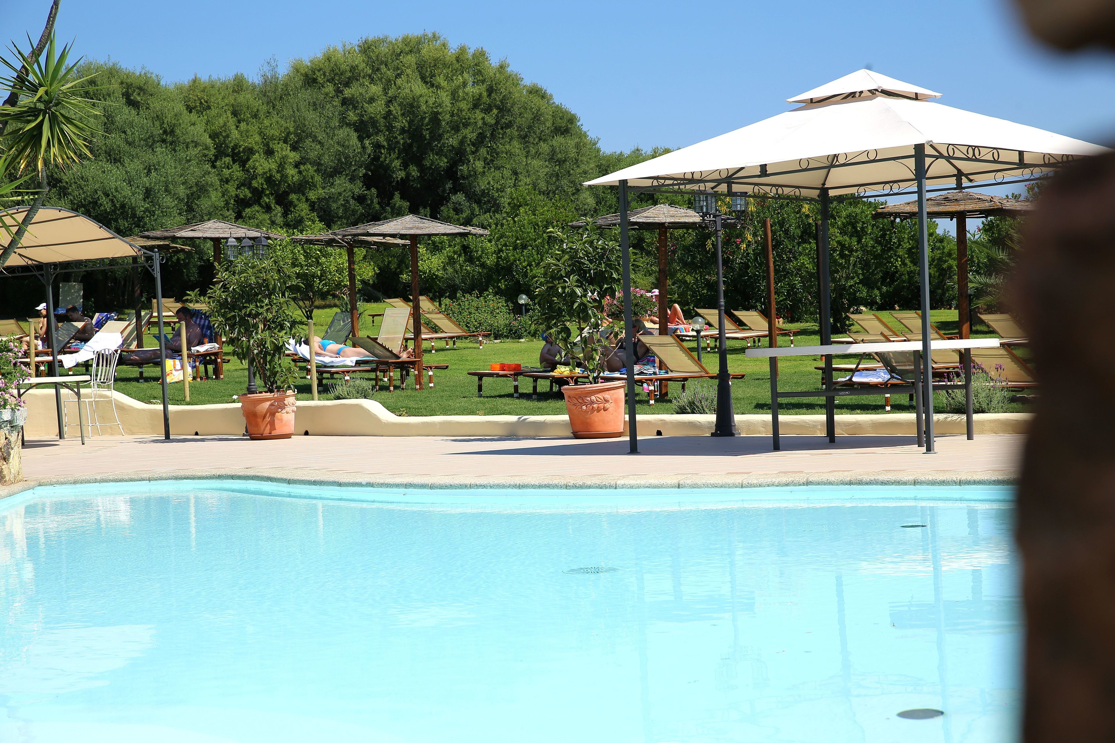 Ein Poolbereich mit Liegestühlen, Sonnenschirmen und einer Laube.