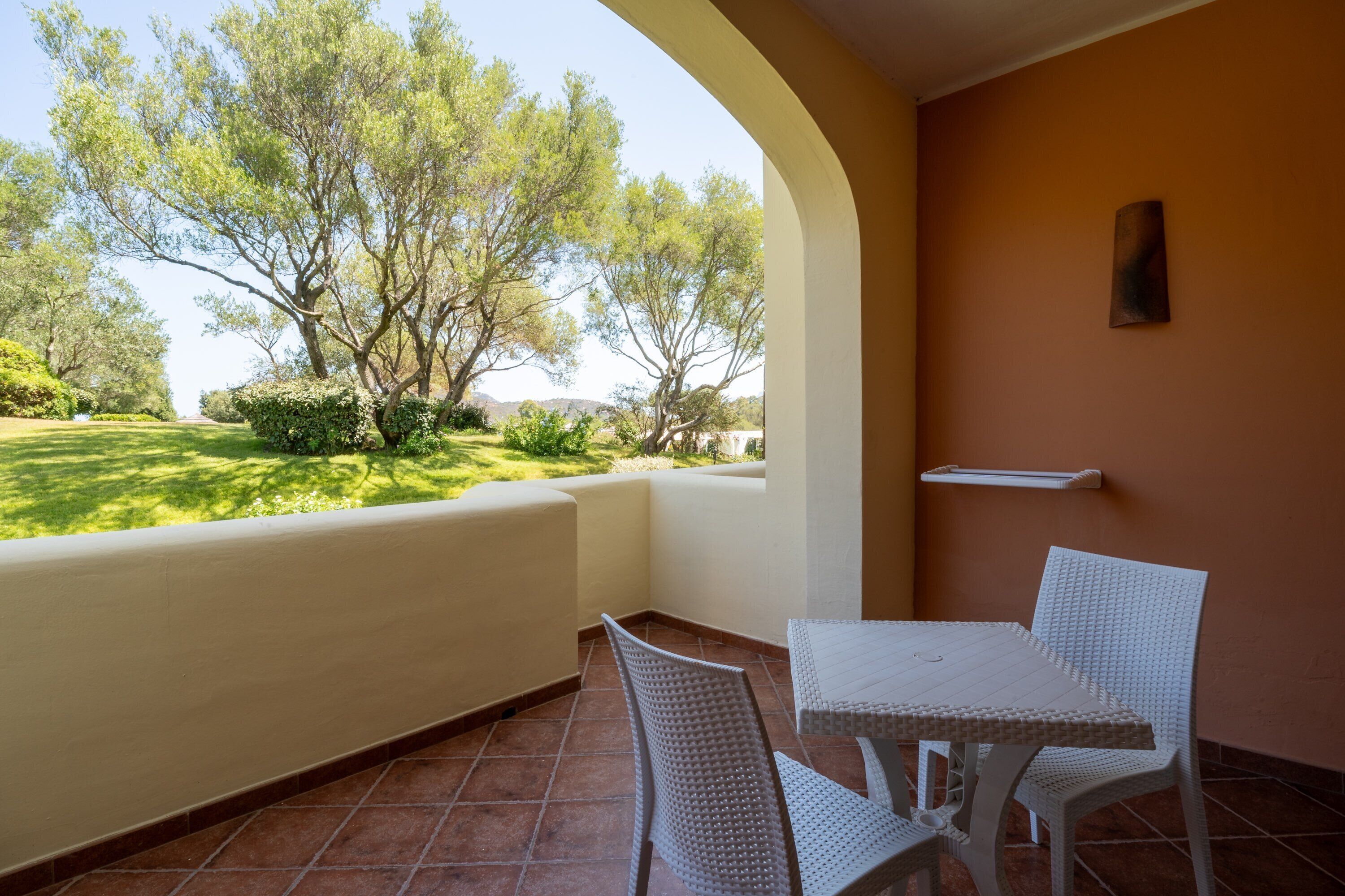 A patio with a white table and chairs, a view of trees, and a wall-mounted shelf.