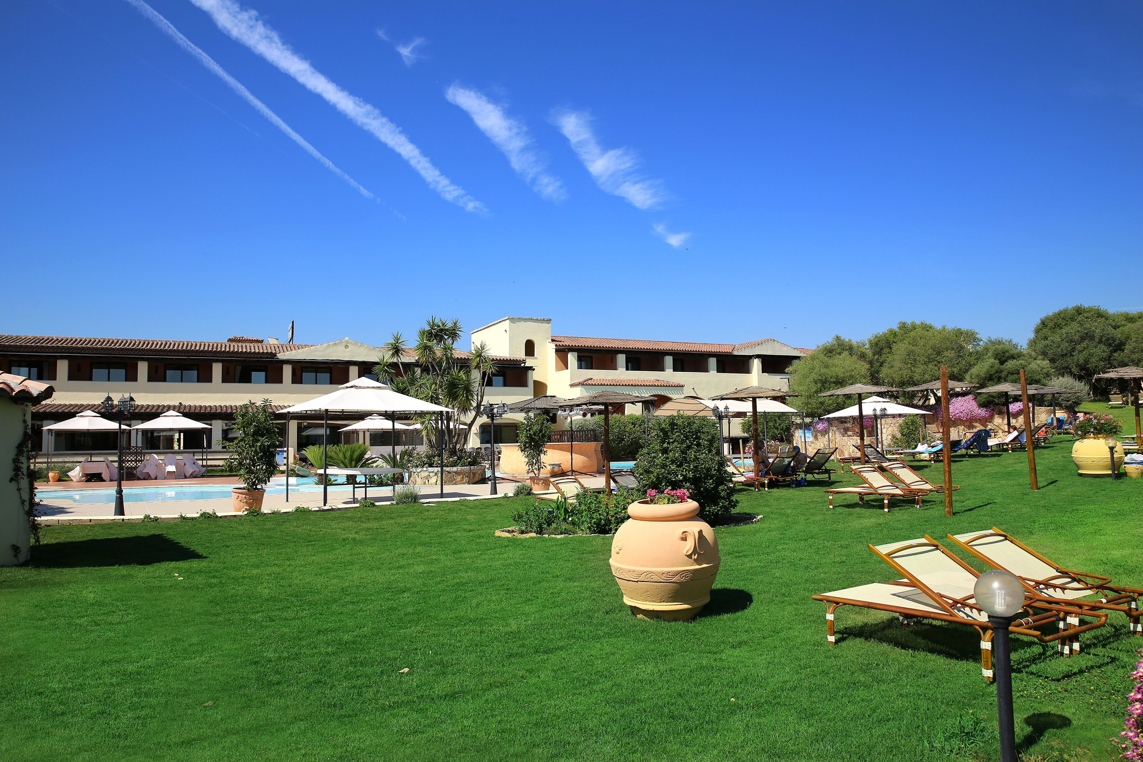 Ein Hotelinnenhof mit Swimmingpool, Liegestühlen, Sonnenschirmen und einem großen Blumentopf.