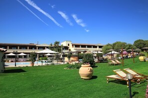 A hotel courtyard with a swimming pool, sun loungers, umbrellas, and a large planter. - Hotel Sa Pedra (Olbia)