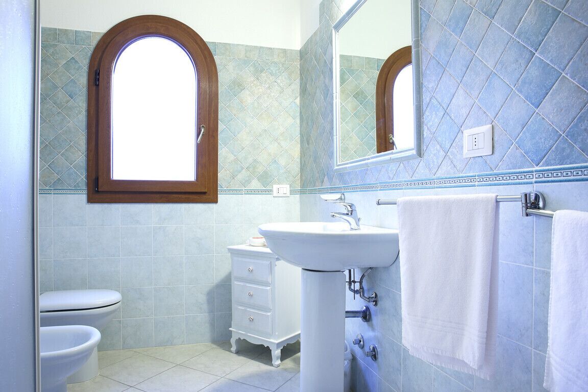 Une salle de bain avec un lavabo blanc, un miroir et une fenêtre.