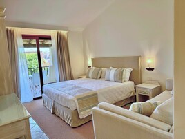 A hotel room with a large bed, a small bedside table, a chair, and a balcony with curtains.
