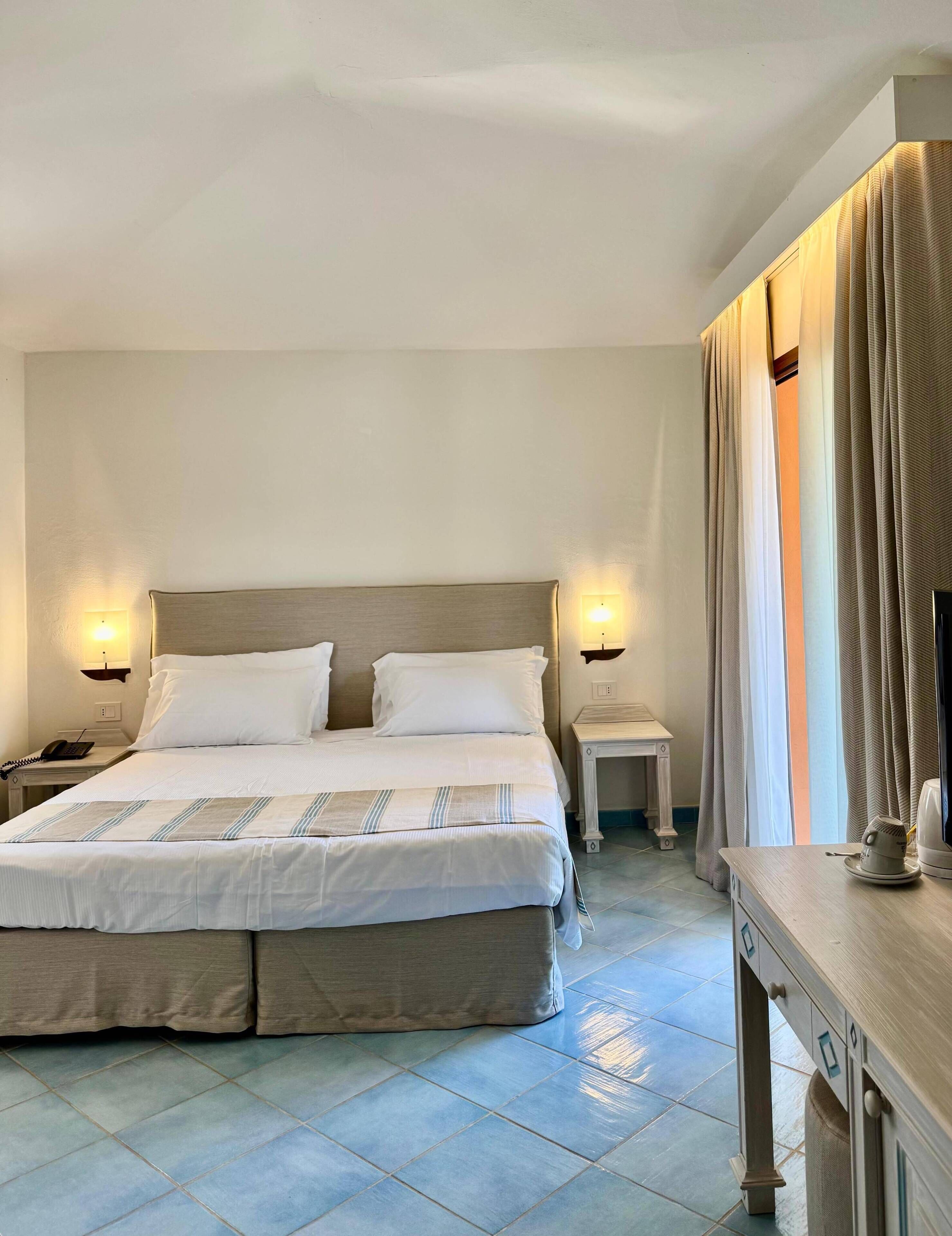 Une chambre d’hôtel avec un grand lit, des lampes de chevet, une table de chevet et un bureau avec une bouilloire.