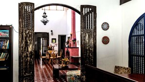 A hallway with patterned flooring, a chandelier, a bookshelf, and a decorative wall. - Hotel 1492 (San José)