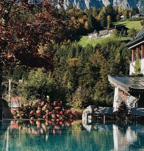 A pool with clear water, surrounded by trees and a mountain backdrop. - Hotel Der Löwe Leogang (Leogang)