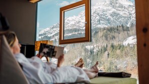 Una persona relajándose en una habitación con un amplio ventanal que da a un paisaje montañoso cubierto de nieve.