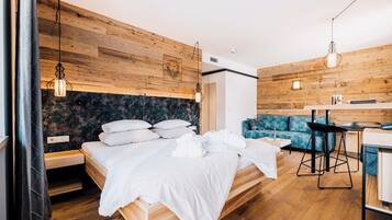 Un dormitorio moderno con cabecera de madera, cama con ropa blanca, sofá azul y una pequeña zona de kitchenette.
