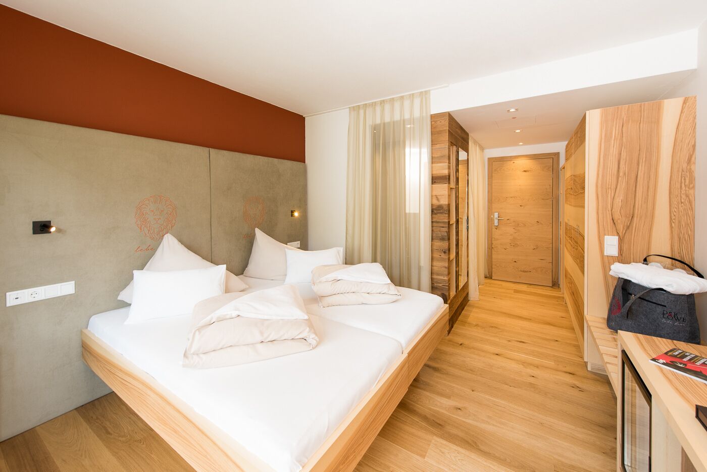 A modern hotel room with a large bed, wooden flooring, a wardrobe, and a visible bathroom door.