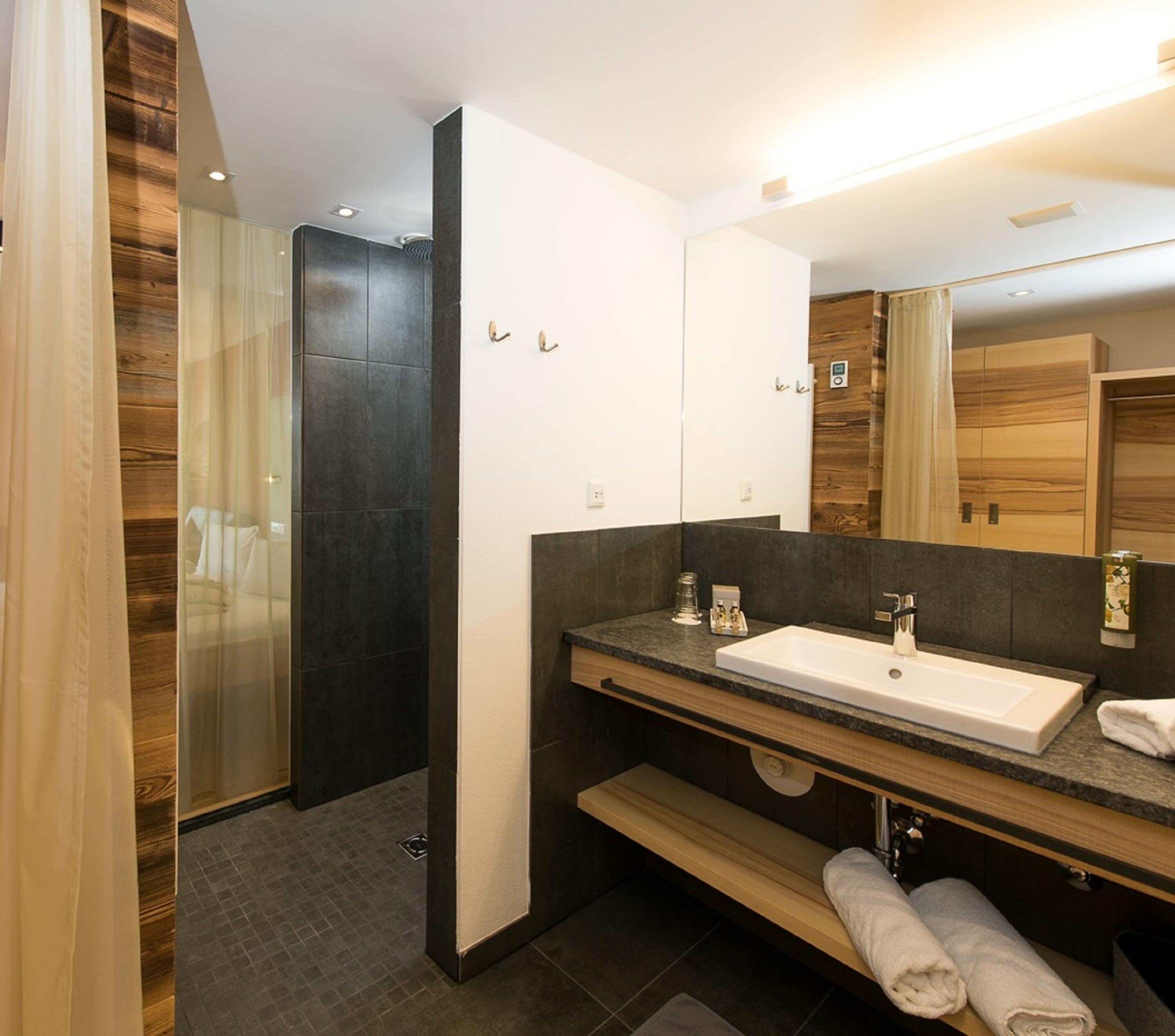 A modern bathroom with a large mirror, dark tiles, and a shower area.