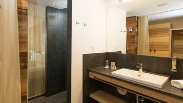 A modern bathroom with a large mirror, dark tiles, and a shower area.