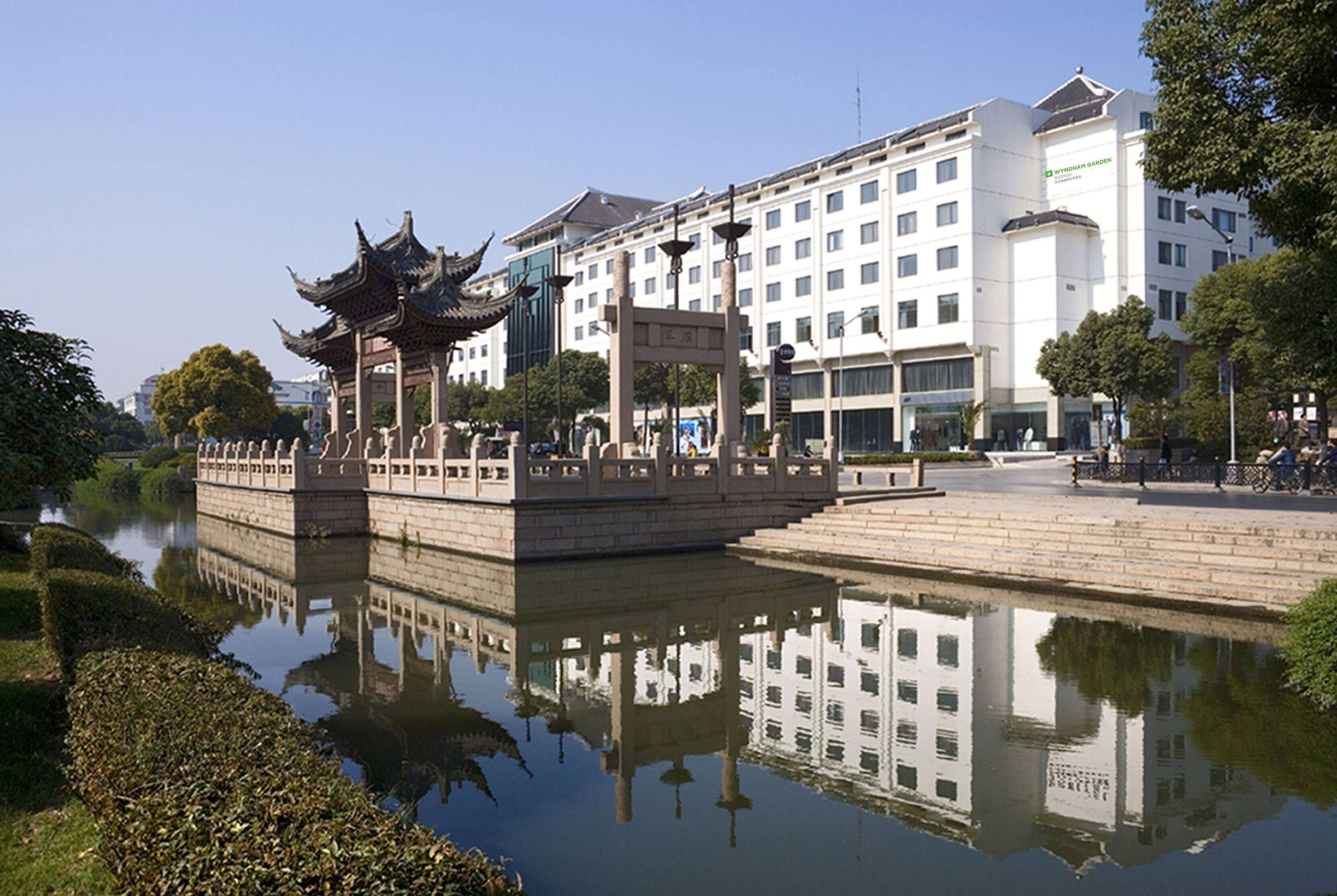 A traditional Chinese pavilion over a reflective water body, with a modern hotel in the background.