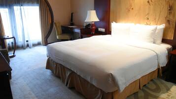 A hotel room with a large bed, a desk, a chair, a lamp, and a painting on the wall.