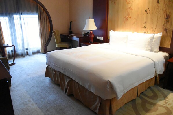 Habitación de hotel con una cama grande, un escritorio, una silla, una lámpara y un cuadro en la pared.