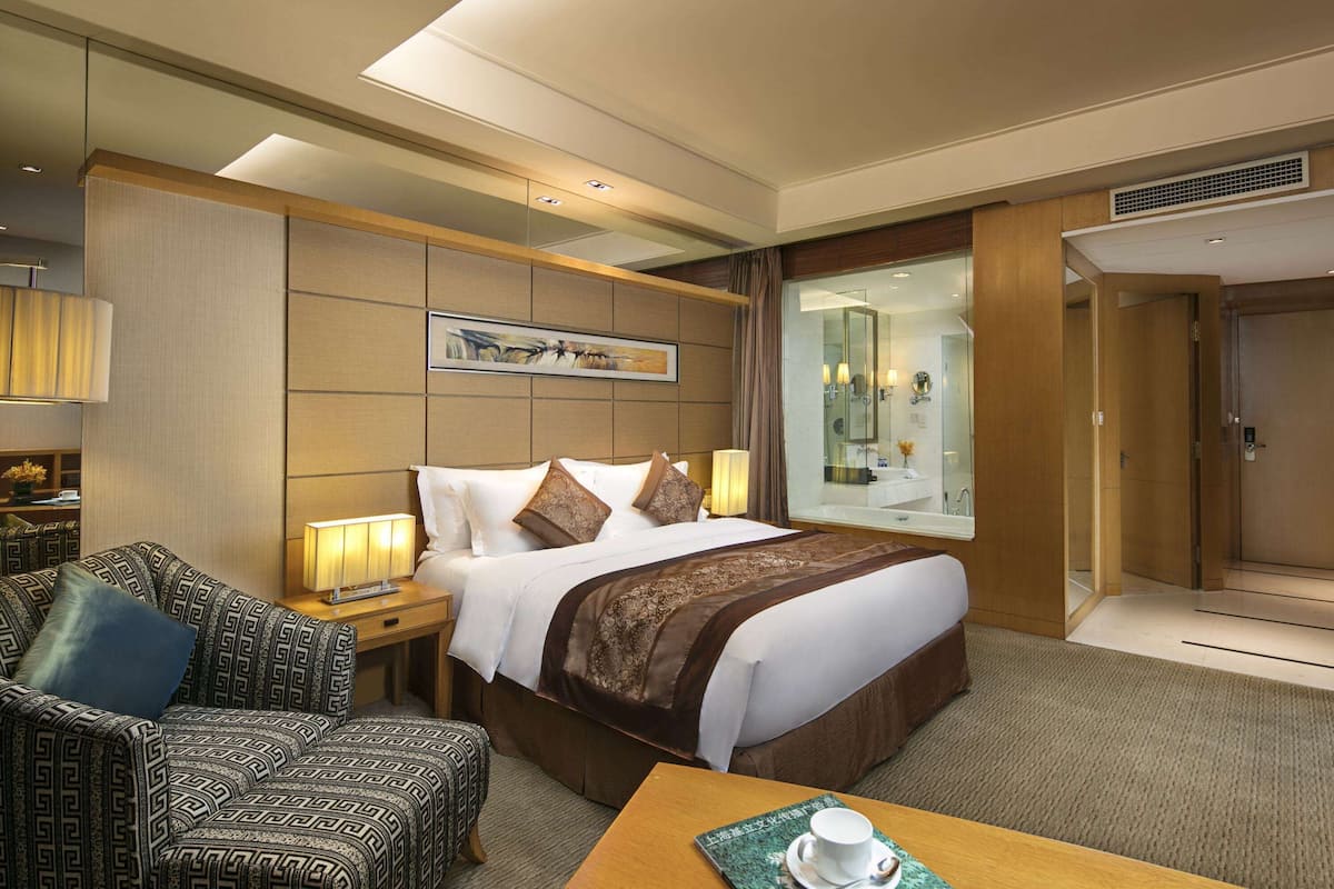 Une chambre d’hôtel avec un grand lit, un canapé, une table basse et une salle de bain visible à travers une porte en verre.