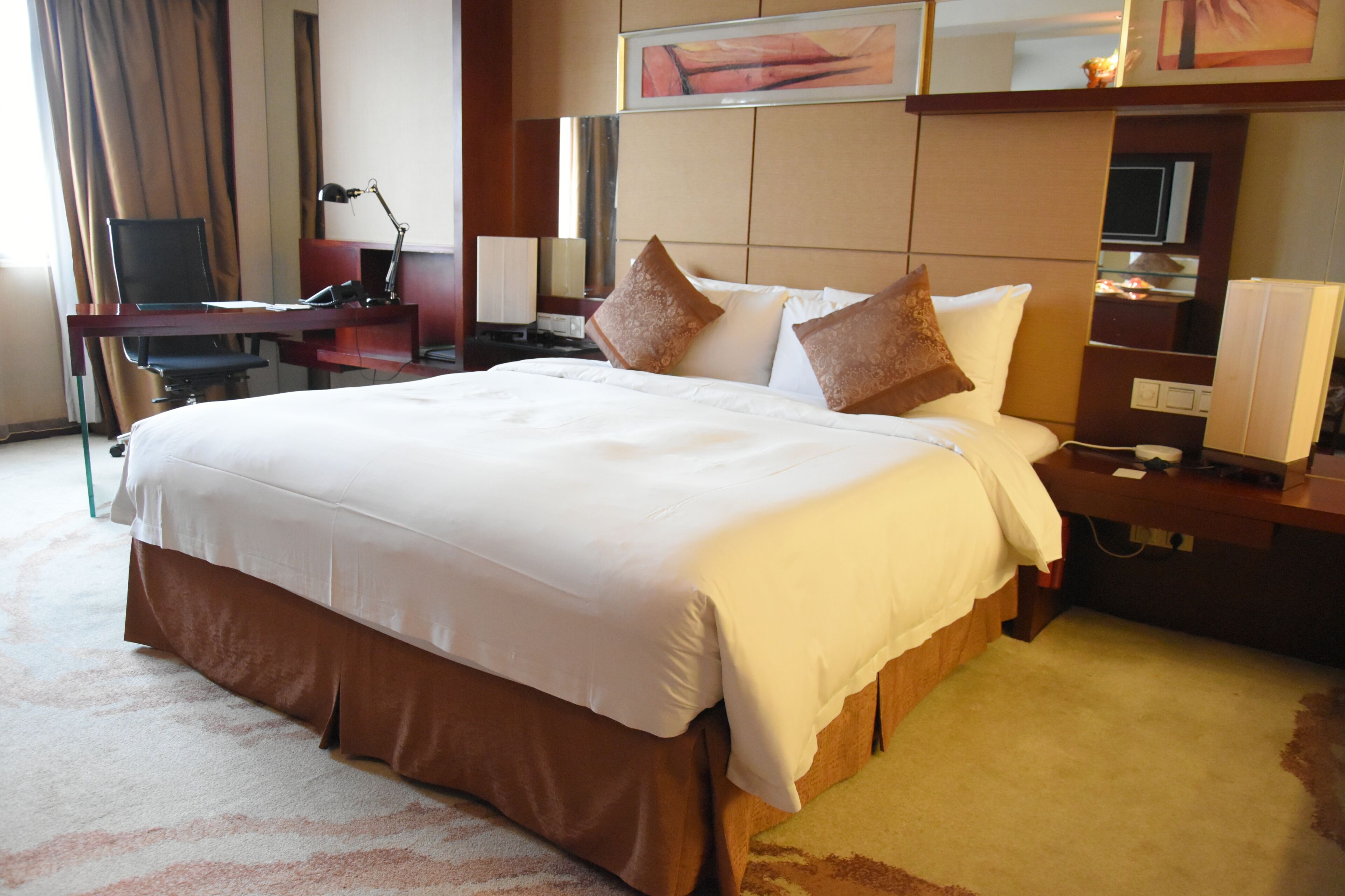 Una habitación de hotel con una cama grande, un escritorio con lámpara y una televisión.