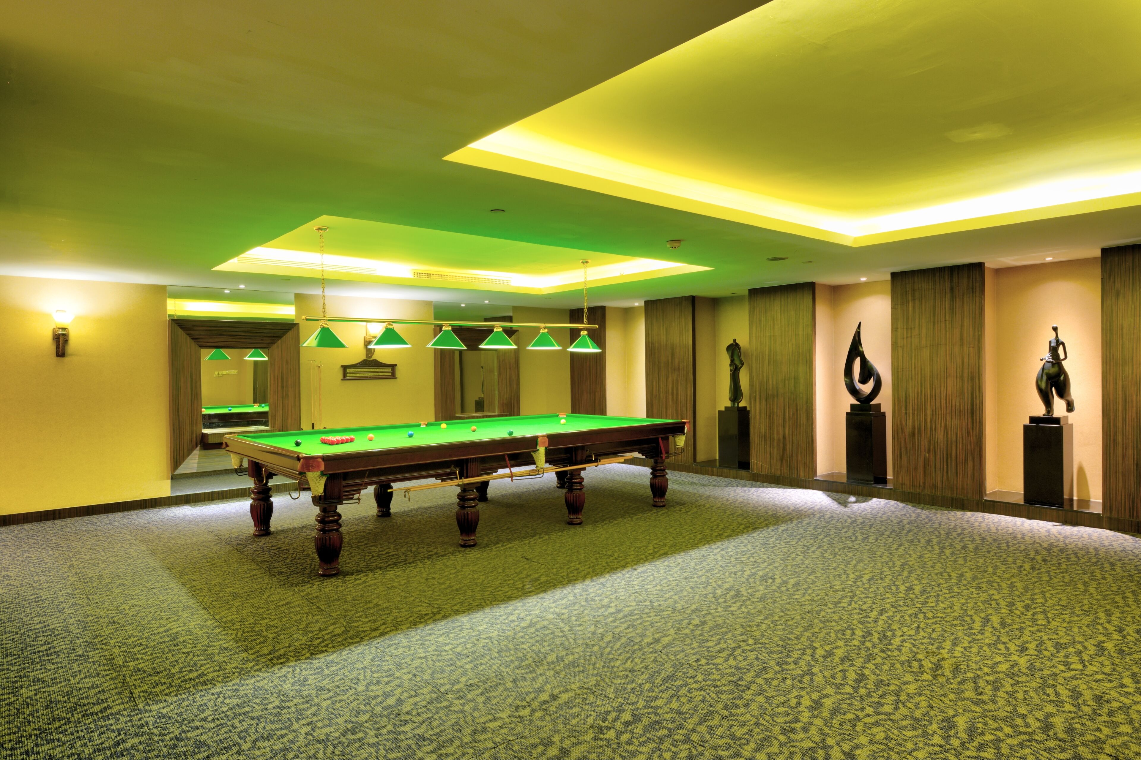 Una mesa de billar en una habitación con piso alfombrado e iluminación verde.