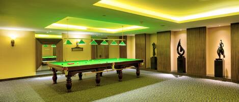 A pool table in a room with a carpeted floor and green lighting.
