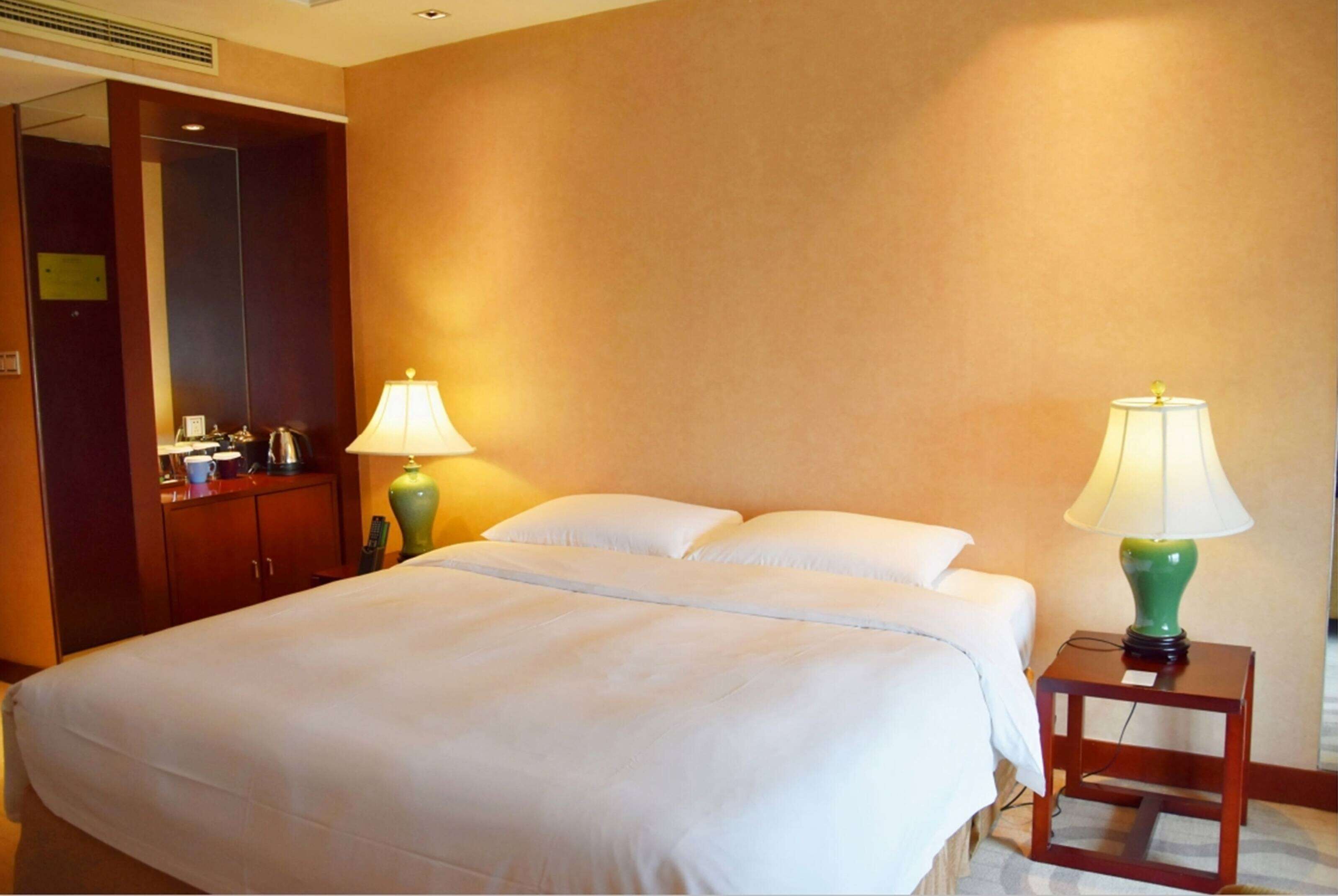 A hotel room with a large bed, two bedside lamps, a wooden nightstand, and a mirror above the bed.