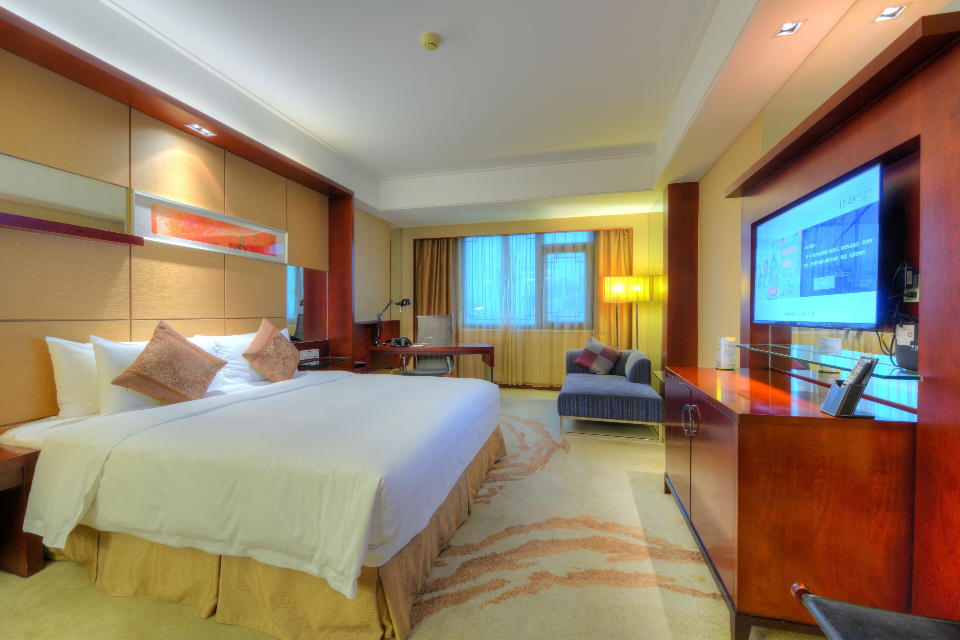 A hotel room with a large bed, a desk, a television, and a seating area.