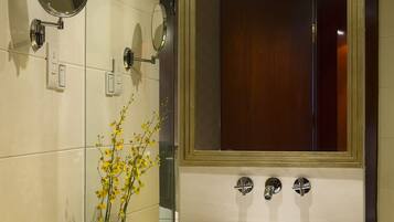 Un baño con un espejo grande, un lavamanos de vidrio y un florero con flores amarillas.
