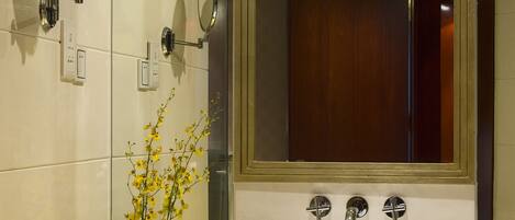 A bathroom with a large mirror, a glass sink, and a vase with yellow flowers.