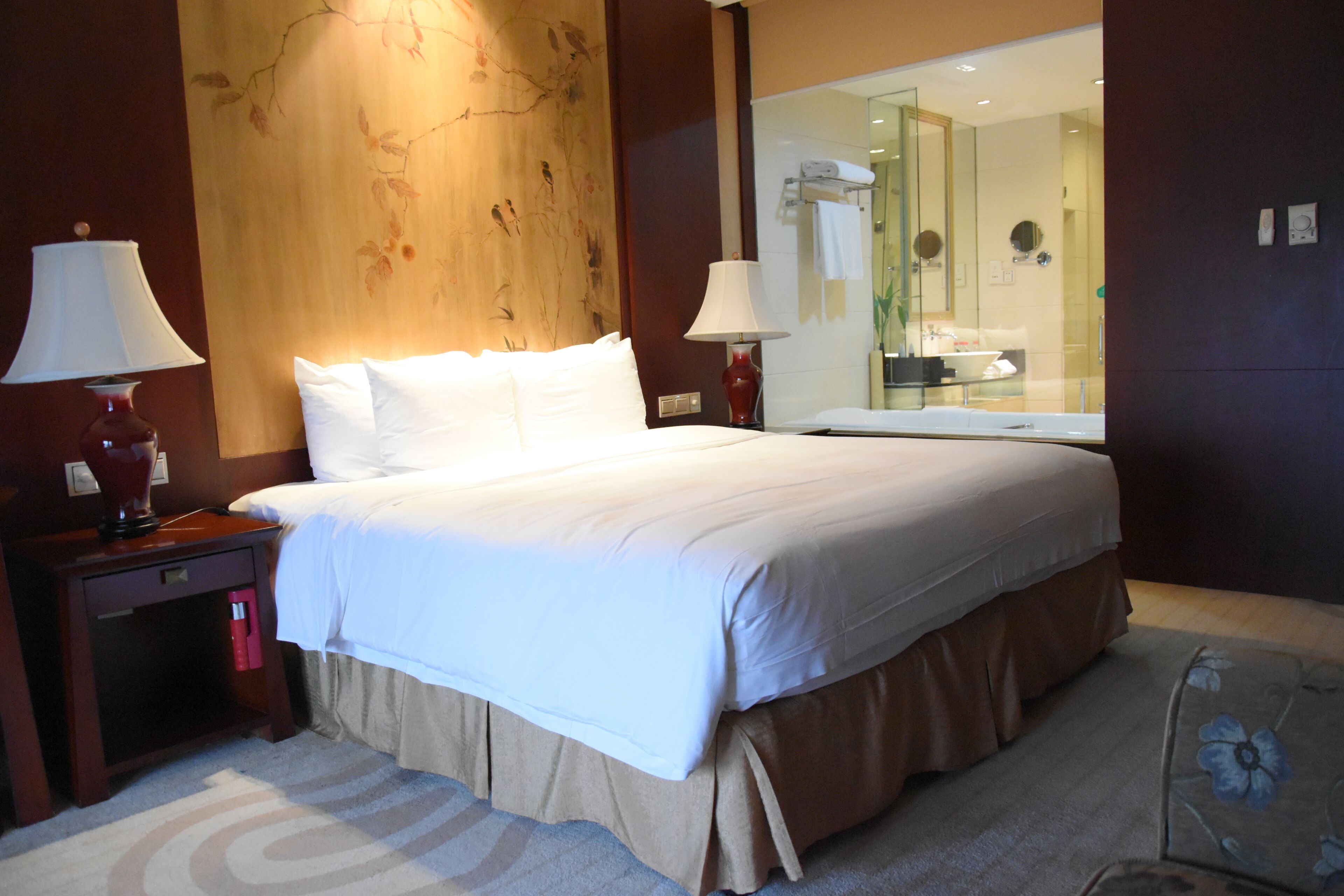 A hotel room with a large bed, two bedside lamps, a nightstand, a mirror, and a carpeted floor.