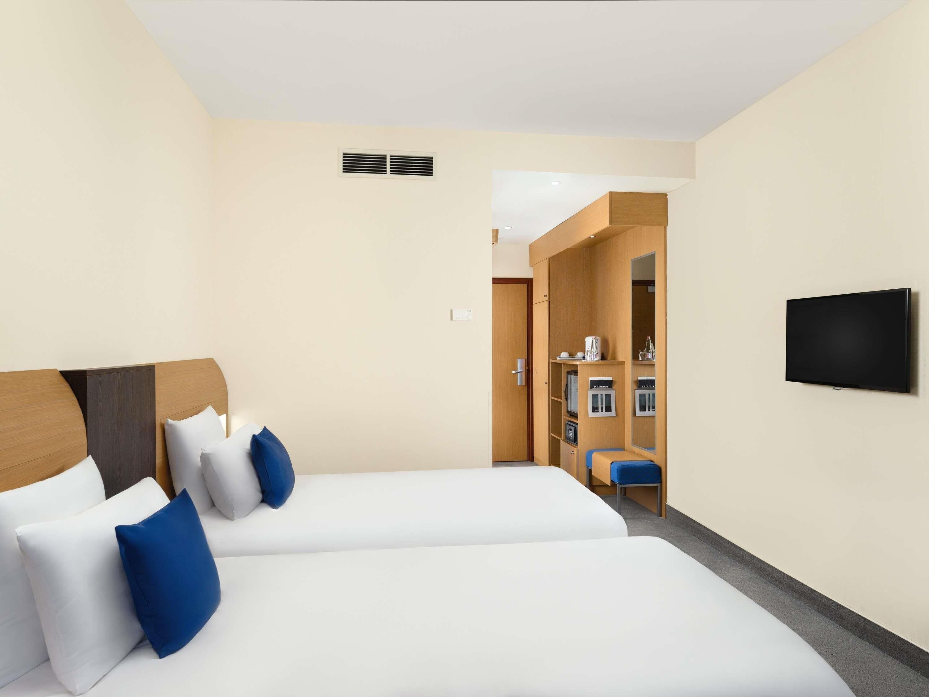 Une chambre d’hôtel avec deux lits, une télévision, une armoire et une salle de bain visible à travers une porte ouverte.