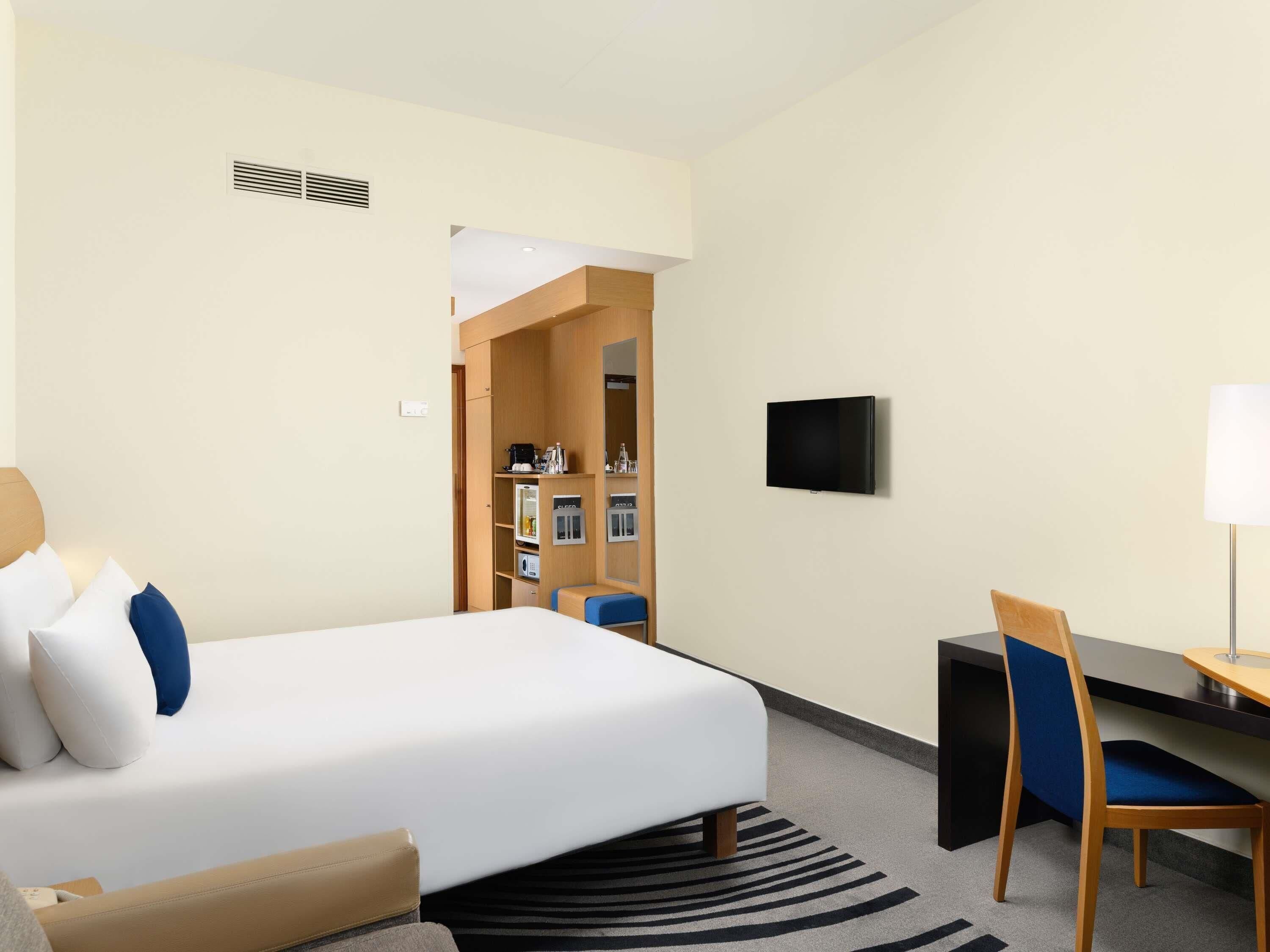 Una habitación de hotel con cama, escritorio, silla, televisor y una zona de kitchenette.