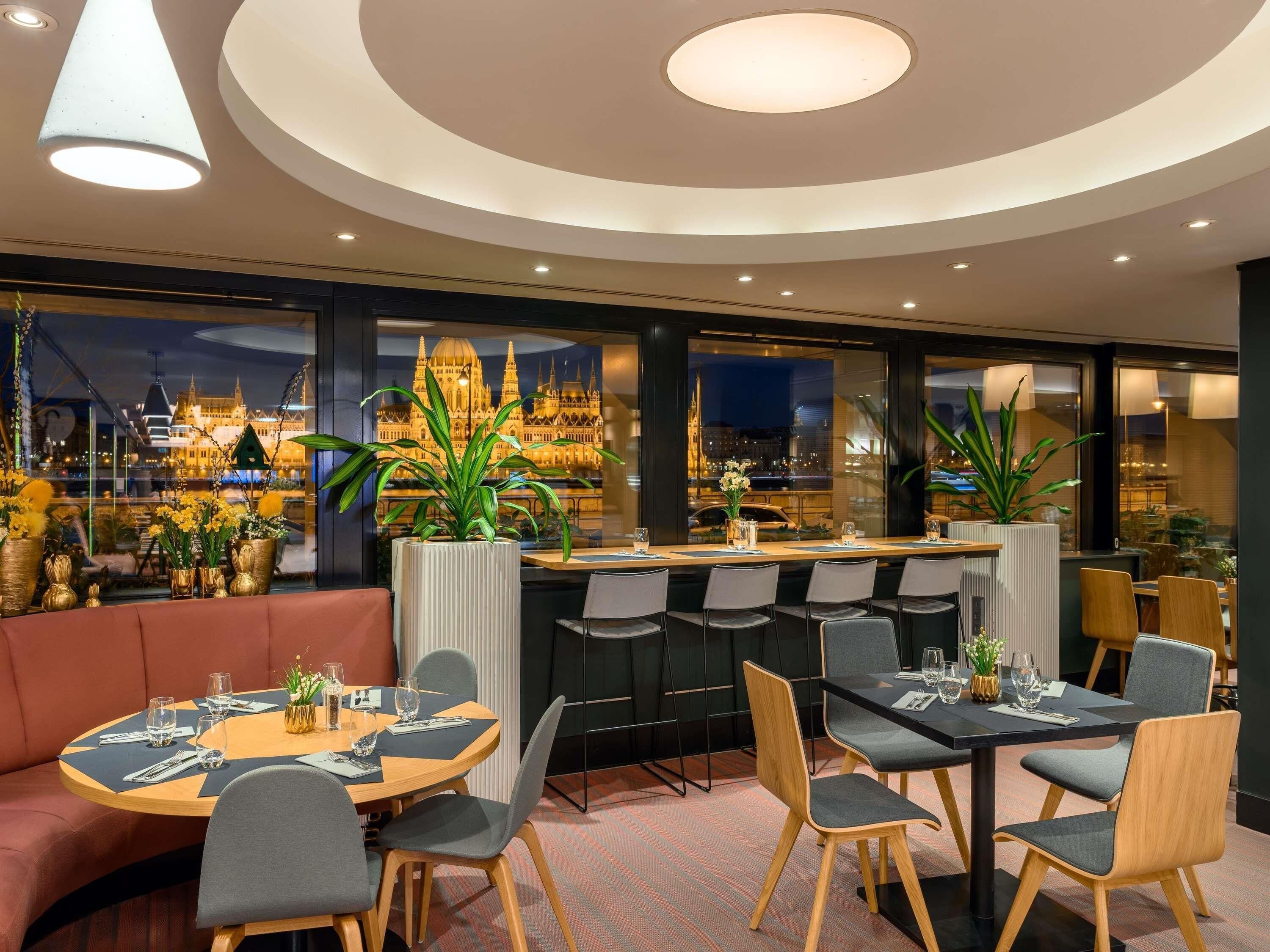 Un restaurante con vista a un edificio histórico, mesas redondas y sillas modernas.