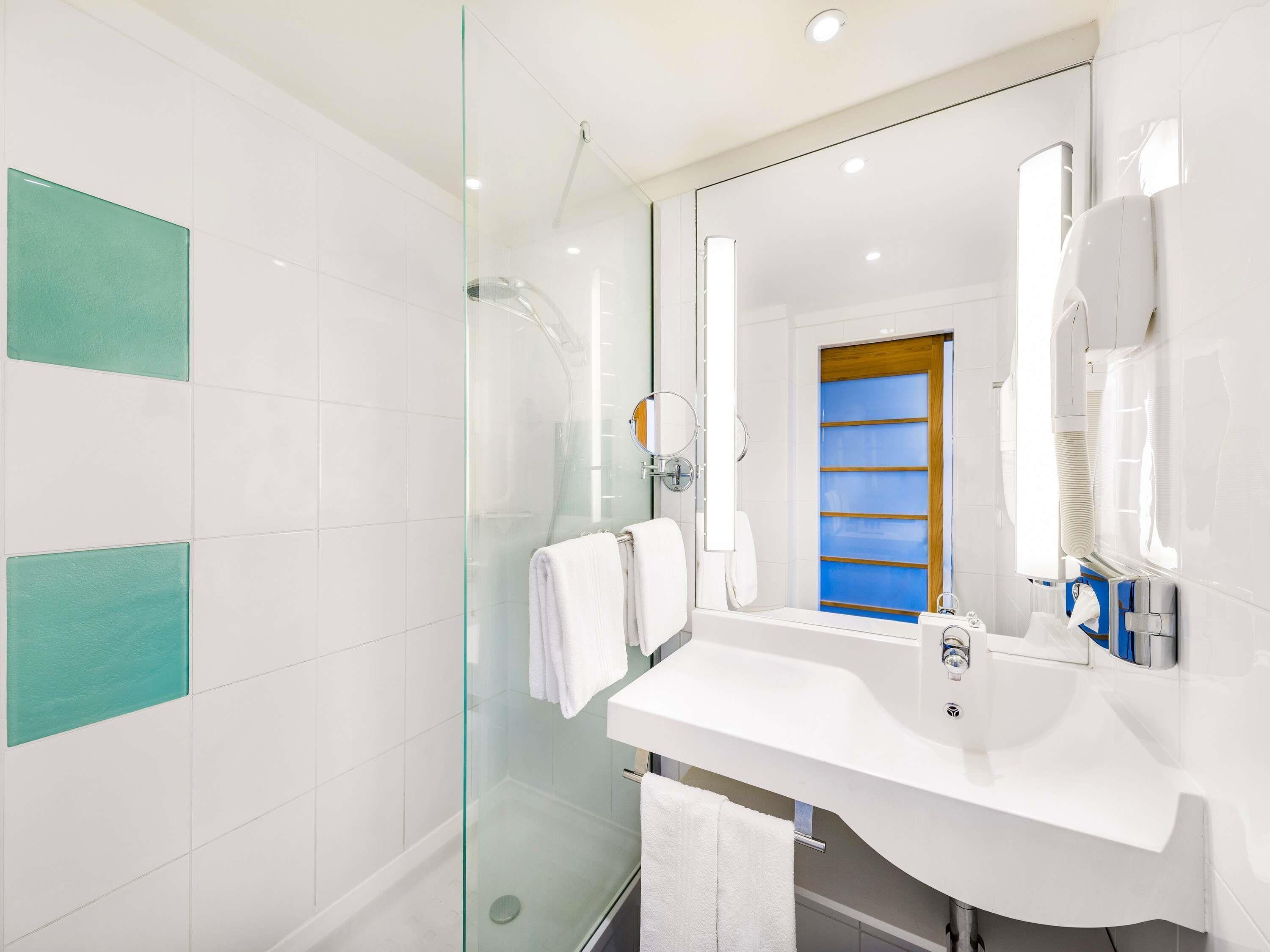Un baño moderno con ducha de vidrio, azulejos blancos y un espejo grande.