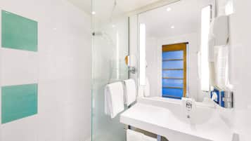 Un baño moderno con ducha de vidrio, azulejos blancos y un espejo grande.