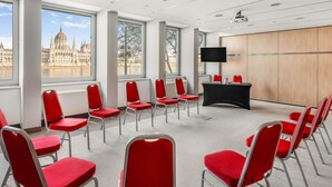 A conference room with red chairs, a black table, and a large window with a view of a historic building. - Novotel Budapest Danube (Budapest)