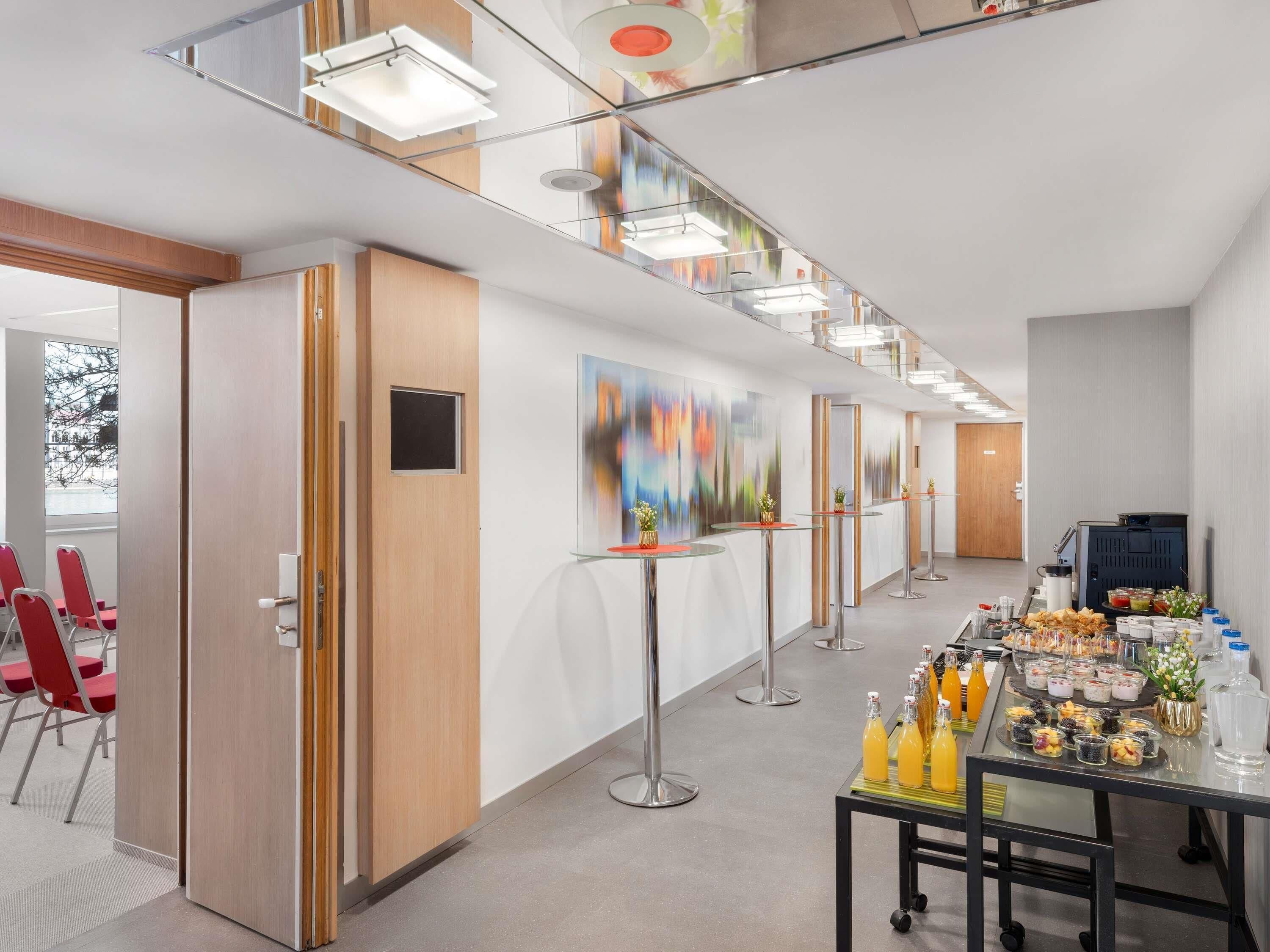 En moderne hotellobby med en lang reception, røde stole og et buffetbord med forskelligt mad.