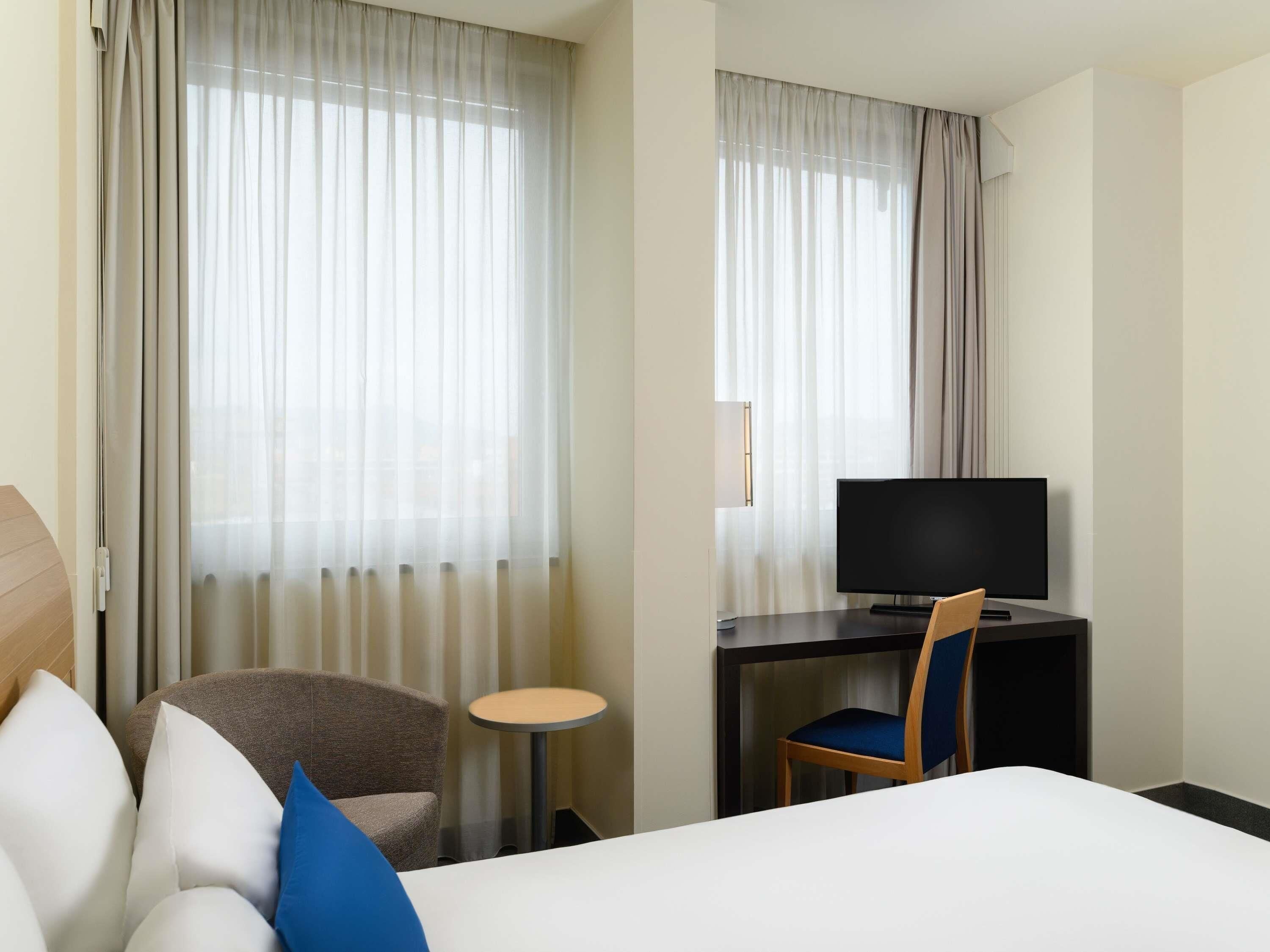 A hotel room with a bed, a TV, a desk, and a chair.