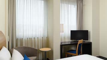 A hotel room with a bed, a TV, a desk, and a chair.