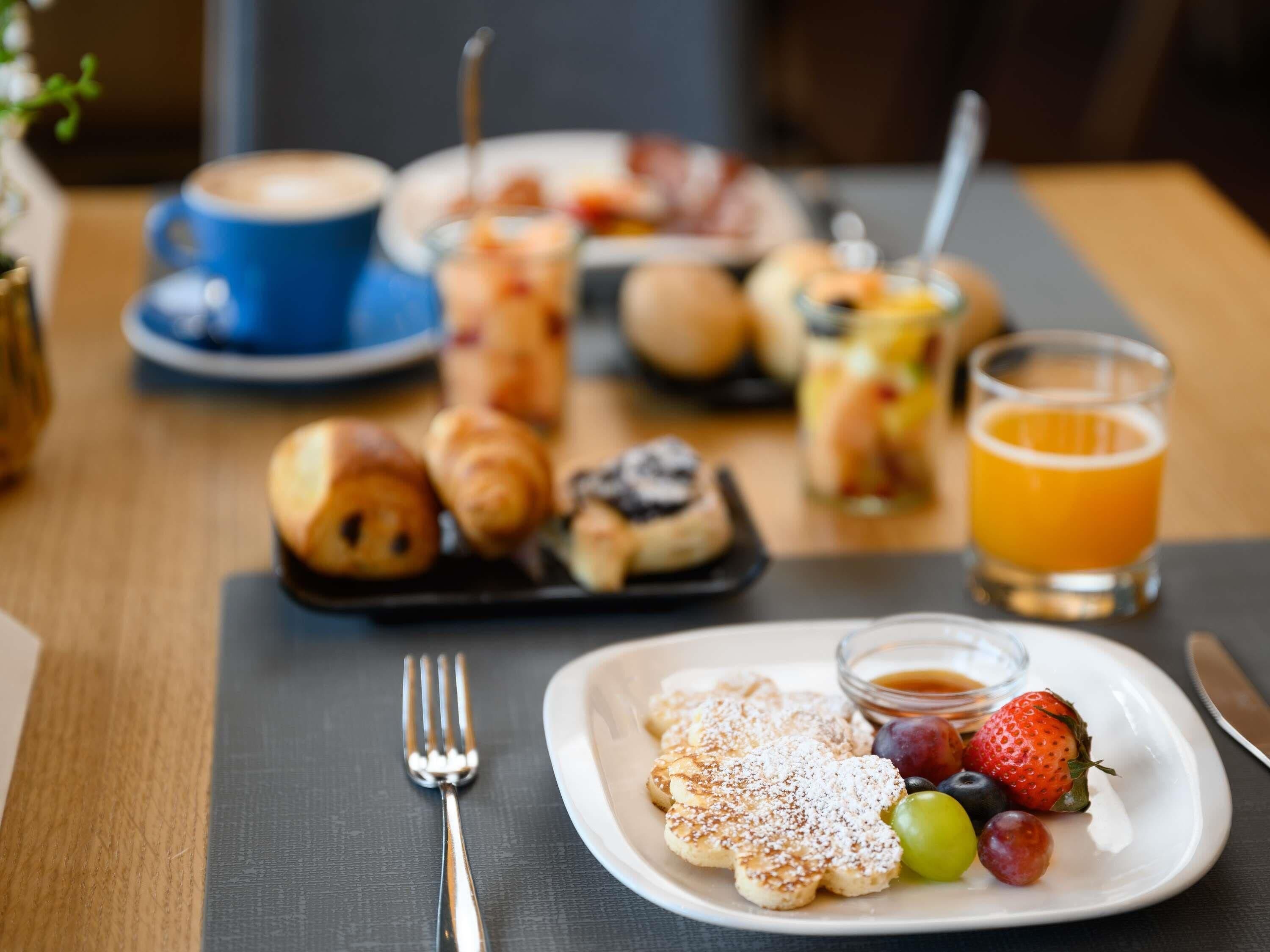 A breakfast setting with pastries, fruits, and a glass of orange juice on a table.