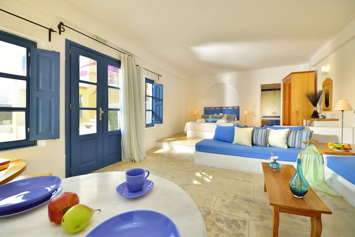 A modern living room with a blue sofa, a wooden coffee table, and a dining area with blue plates and fruit.