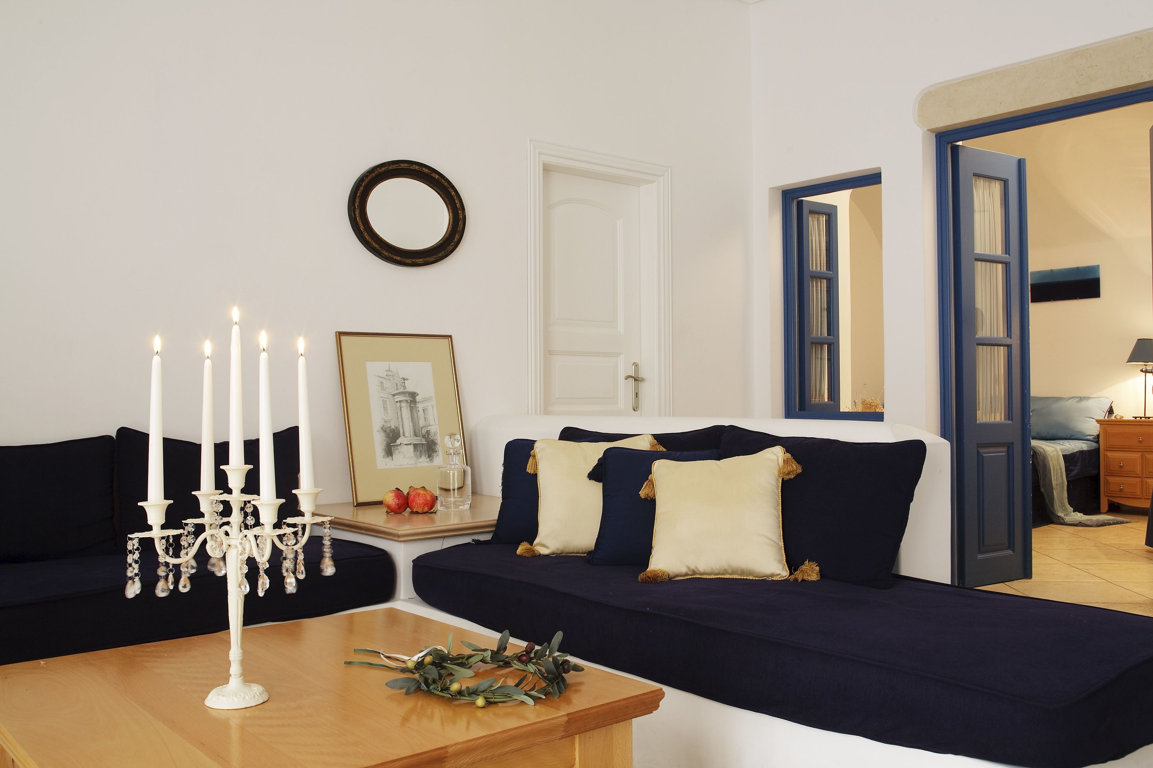 Ein Wohnzimmer mit einem dunkelblauen Sofa, einer weißen Wand, einem Holztisch mit einem Kandelaber und einer Tür zu einem anderen Raum.