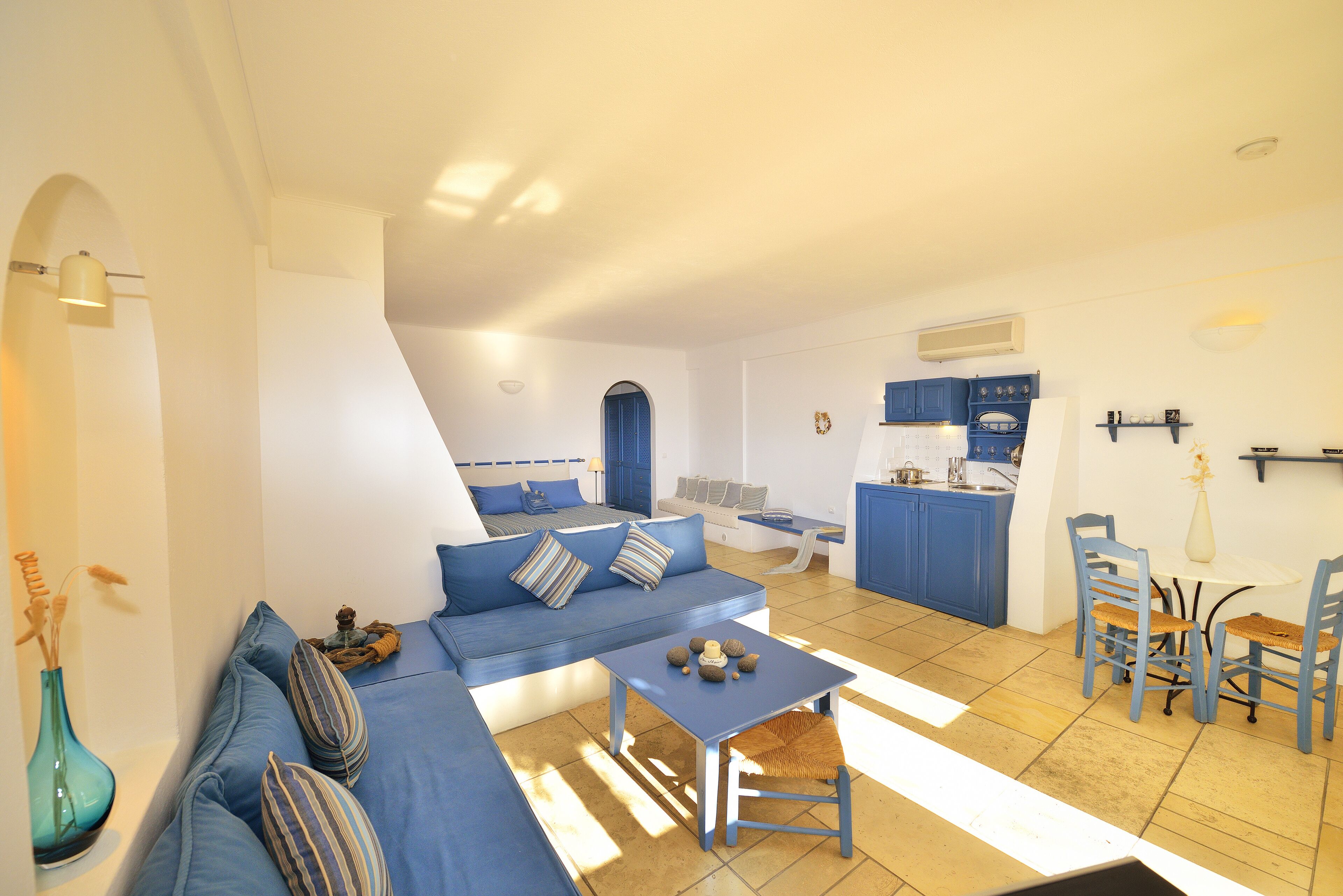 A modern living room with a sofa, a small table, and a kitchen area with blue cabinets and a dining table.