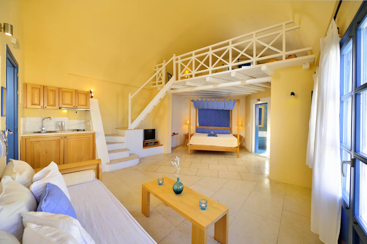 A spacious living area with a staircase, a bed, a sofa, and a small table with candles.