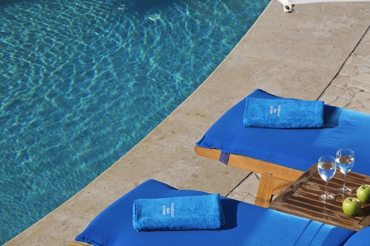 A poolside lounge area with blue towels and a tray with glasses and apples.
