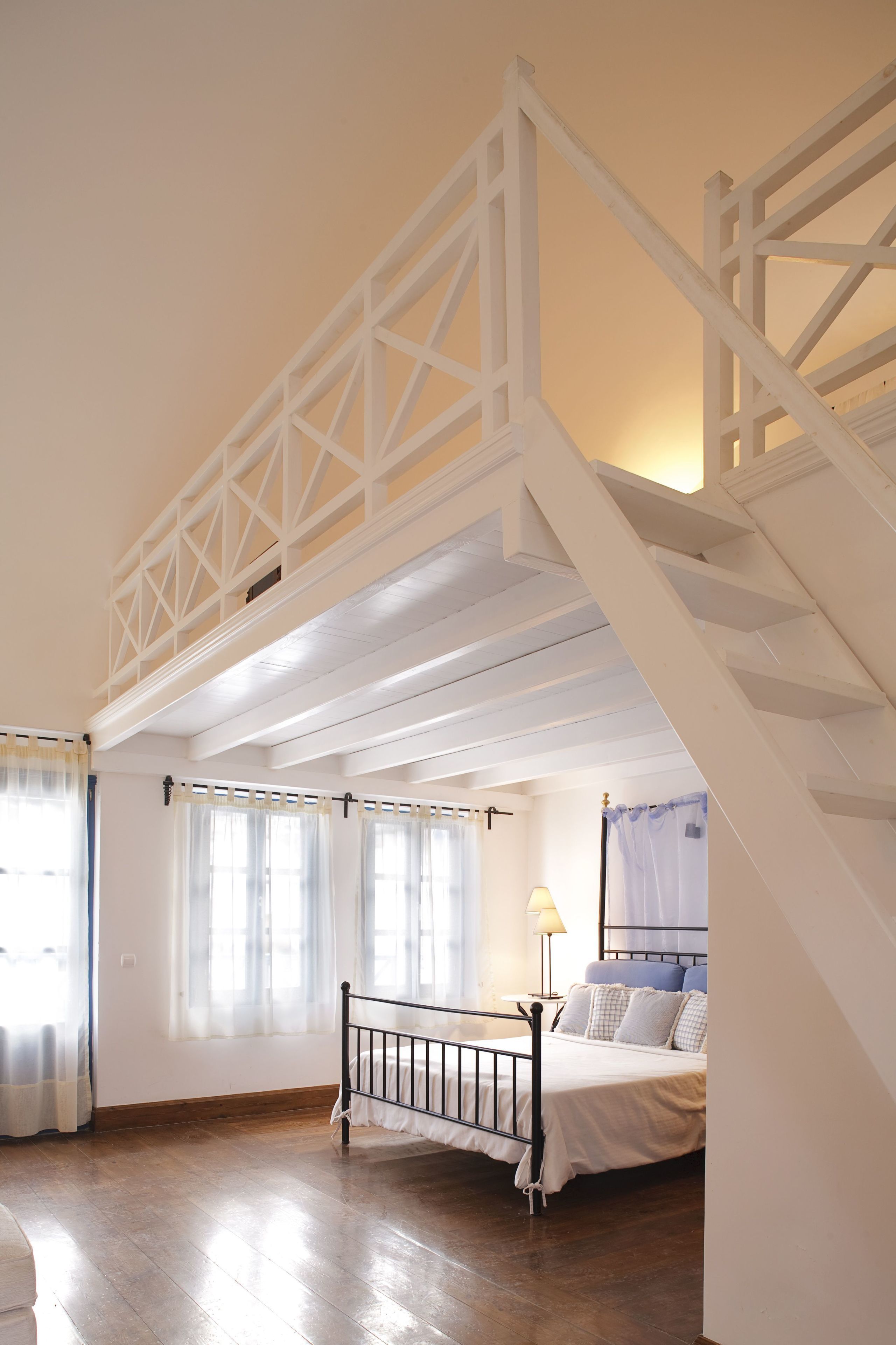 Ein Schlafzimmer mit Holzboden, einem Bett mit weißer Bettwäsche, einem Nachttisch und einem Fenster mit Vorhängen.